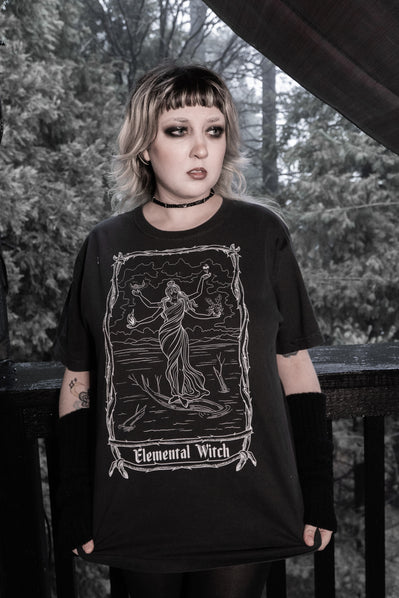 Person wearing the Elemental Witch Tee by The Pretty Cult, black cotton witch graphic t-shirt styled outdoors